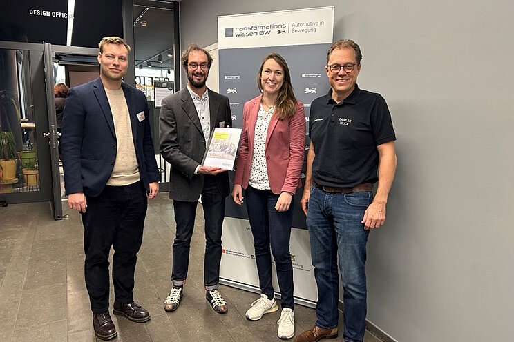 Vier Personen blicken lächelnd in die Kamera und halten dabei eine neue Studie von e-mobil BW hoch.